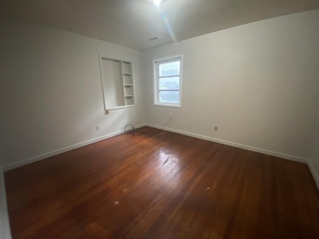 empty room featuring dark wood-style flooring, baseboards, and built in features