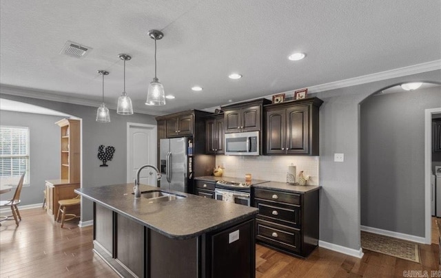 1210 Skyline Dr, Sheridan, AR 72150 - kitchen with appliances with stainless steel finishes, a sink, arched walkways, dark countertops, and a center island with sink
