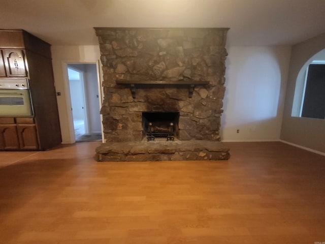 1008 W A Ave, North Little Rock, AR 72116 - unfurnished living room with wood finished floors, a stone fireplace, and arched walkways