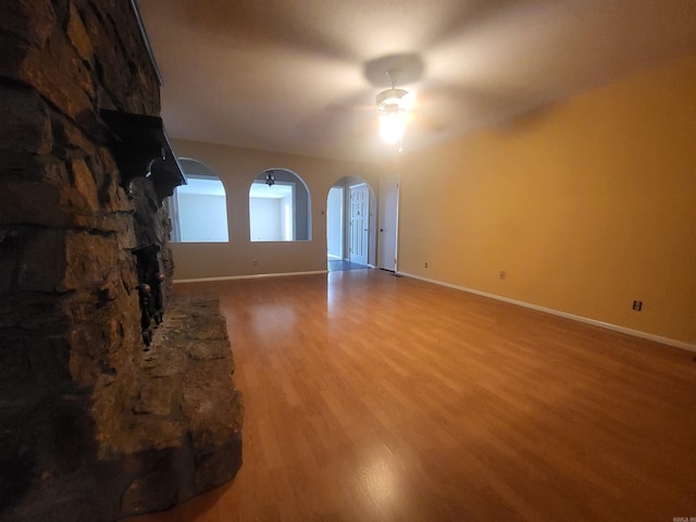 1008 W A Ave, North Little Rock, AR 72116 - unfurnished living room with a ceiling fan, arched walkways, wood finished floors, and a stone fireplace