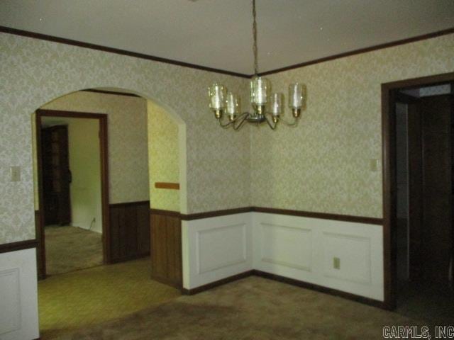 carpeted spare room with wallpapered walls, a wainscoted wall, a chandelier, arched walkways, and crown molding