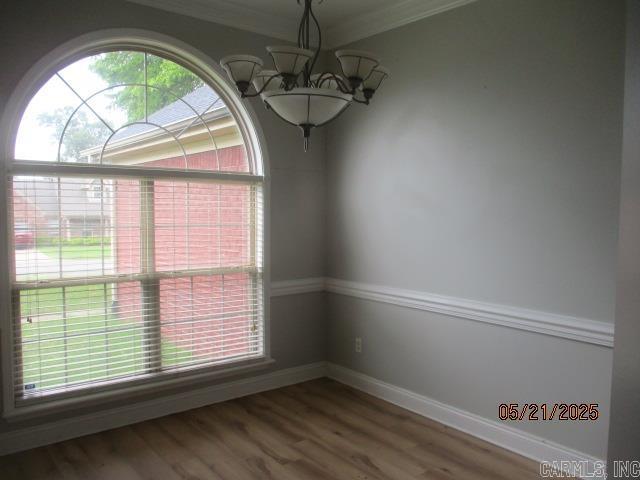 empty room featuring a chandelier, wood finished floors, and ornamental molding