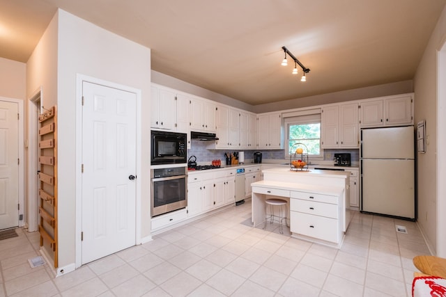 10 Cedar Branch Dr, Little Rock, AR 72223 - kitchen featuring stainless steel oven, freestanding refrigerator, black microwave, under cabinet range hood, and white cabinetry