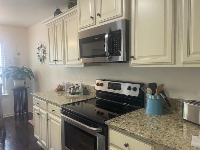 kitchen with stainless steel appliances, light stone counters, dark wood-type flooring, and cream cabinetry