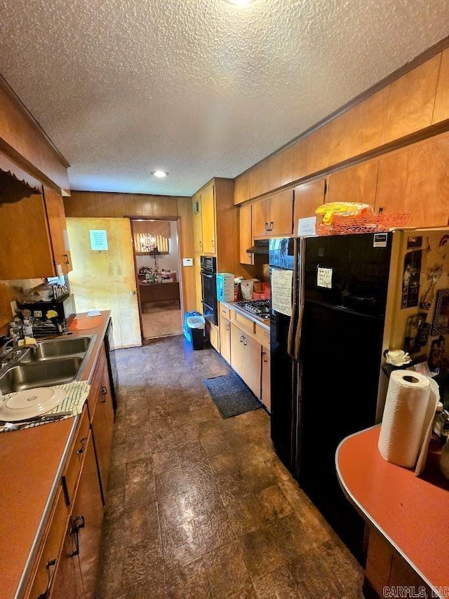 kitchen with freestanding refrigerator, stainless steel gas cooktop, a textured ceiling, brown cabinetry, and wooden walls