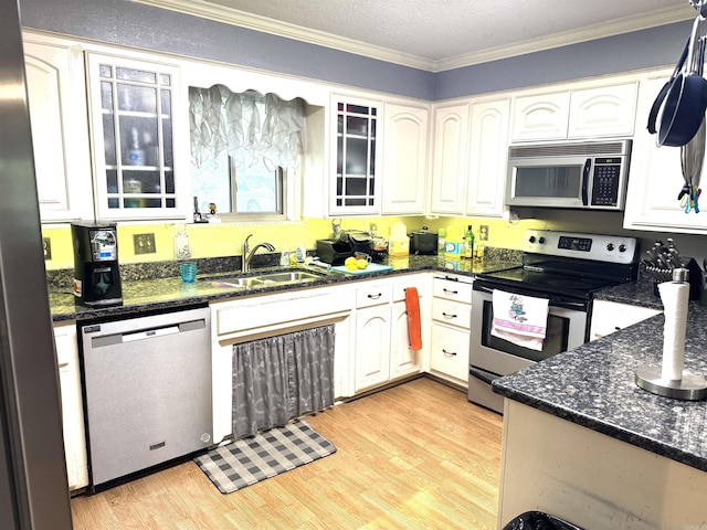 kitchen with appliances with stainless steel finishes, ornamental molding, white cabinets, light wood-style floors, and dark stone counters