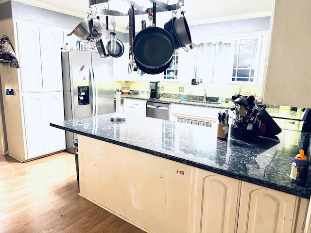 kitchen with crown molding, appliances with stainless steel finishes, light wood-type flooring, dark stone countertops, and white cabinetry