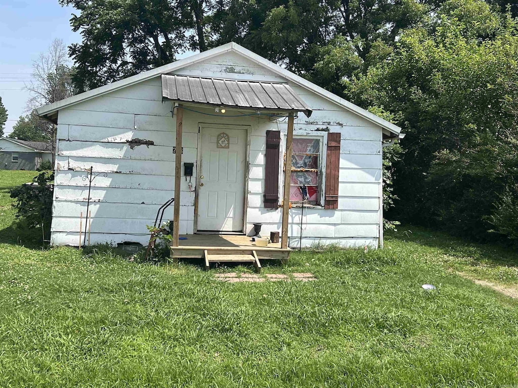 768 E Locust, Piggott, AR 72454 - view of front of house featuring a front lawn, a metal roof, an outdoor structure, and a standing seam roof