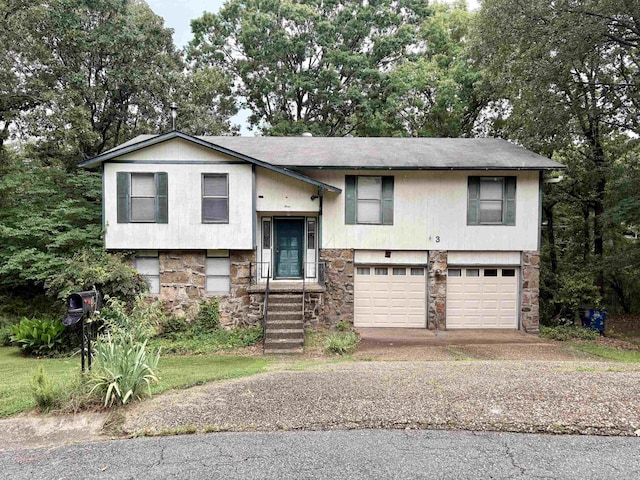 bi-level home featuring stone siding, an attached garage, and asphalt driveway