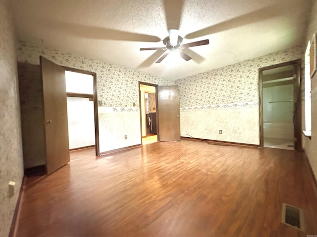 empty room with wallpapered walls, wood finished floors, ceiling fan, and wainscoting