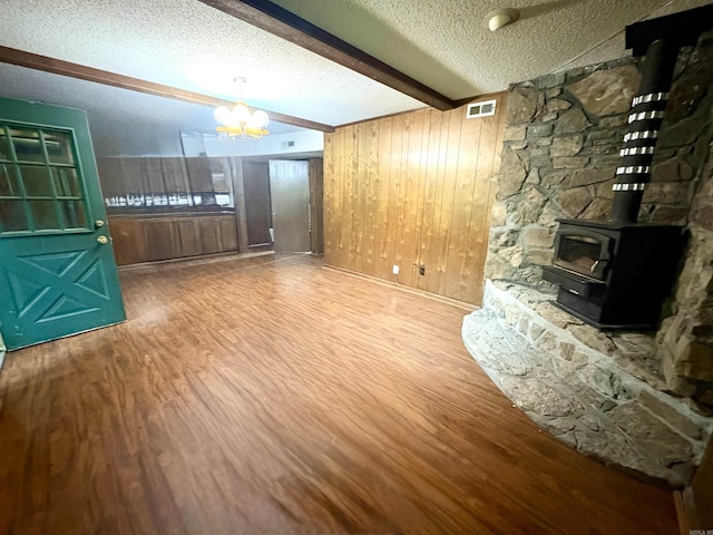unfurnished living room with wood finished floors, beamed ceiling, a chandelier, a textured ceiling, and a wood stove