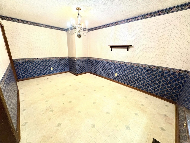 empty room featuring wallpapered walls, a wainscoted wall, a chandelier, tile patterned floors, and a textured ceiling