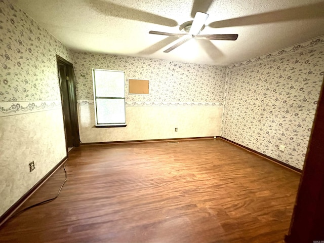 unfurnished room featuring wood finished floors, wallpapered walls, a ceiling fan, and a textured ceiling