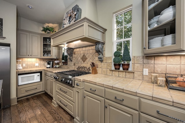 12 Cobblestone Way, Little Rock, AR 72223 - kitchen with appliances with stainless steel finishes, glass insert cabinets, dark wood-style flooring, light countertops, and decorative backsplash