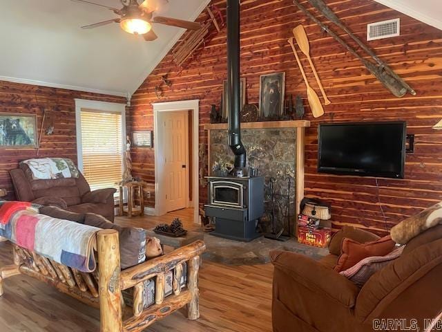 living area with wood finished floors, ceiling fan, a wood stove, and wood walls