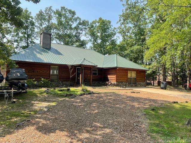 rear view of house featuring driveway, a chimney, and a metal roof