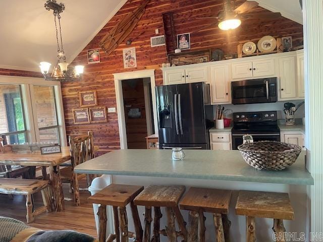 kitchen featuring black appliances, wooden walls, a breakfast bar, decorative light fixtures, and wood finished floors