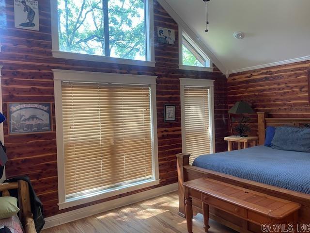 bedroom with wooden walls, wood finished floors, and high vaulted ceiling