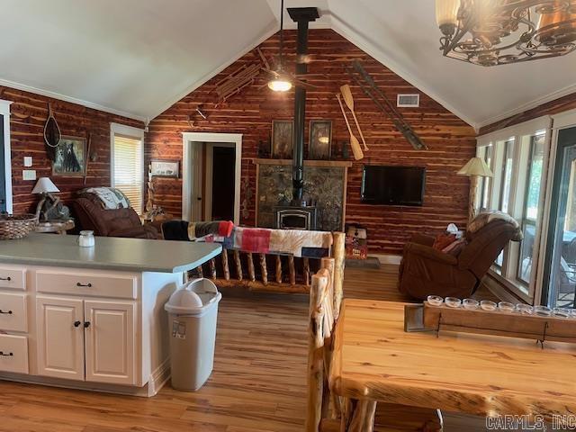 dining space featuring a wood stove, lofted ceiling, light wood finished floors, a chandelier, and wooden walls