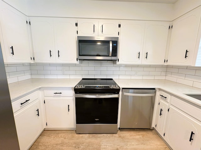 kitchen with appliances with stainless steel finishes, light wood-style floors, white cabinets, and backsplash