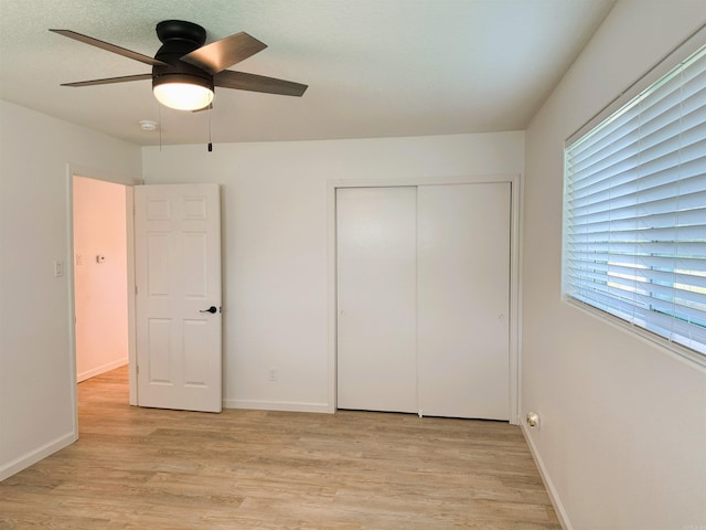 unfurnished bedroom with light wood-style flooring, a closet, multiple windows, and a ceiling fan