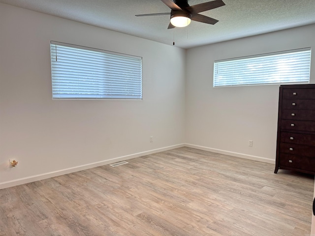 unfurnished room with ceiling fan, light wood finished floors, and a textured ceiling