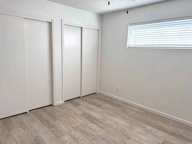 unfurnished bedroom featuring multiple closets, light wood finished floors, and a textured ceiling