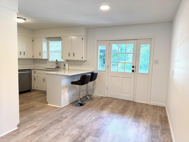 kitchen featuring stainless steel dishwasher, a kitchen bar, light wood finished floors, white cabinetry, and a textured ceiling