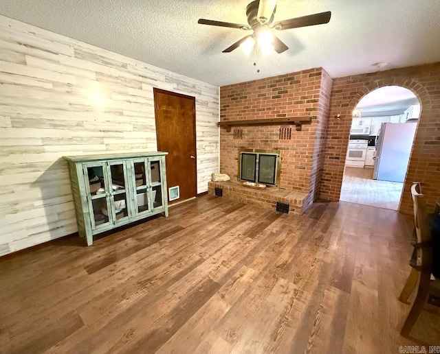 1711 Lonoke Rd, Mountain Home, AR 72653 - unfurnished living room featuring ceiling fan, wood finished floors, a textured ceiling, a fireplace, and arched walkways
