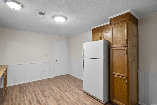 503 N Walnut St, Searcy, AR 72143 - kitchen featuring freestanding refrigerator, light wood finished floors, brown cabinetry, wainscoting, and a textured ceiling