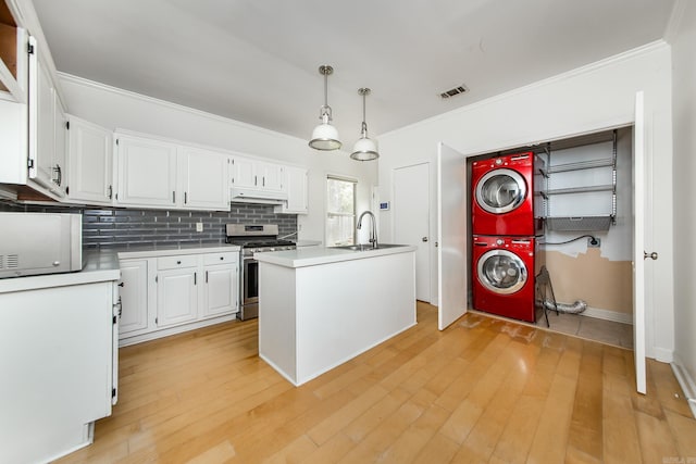4106 C St, Little Rock, AR 72205 - kitchen featuring stainless steel range with gas cooktop, stacked washer / drying machine, white cabinetry, ornamental molding, and a center island with sink
