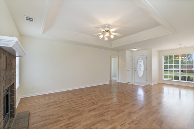 unfurnished living room with a fireplace, a tray ceiling, ceiling fan, light wood-style floors, and a chandelier