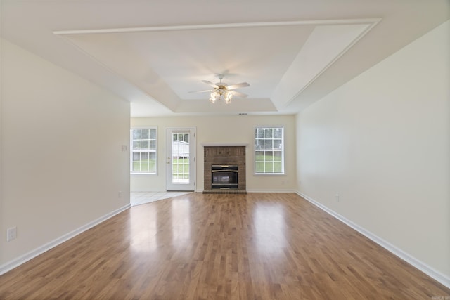 unfurnished living room featuring a raised ceiling, wood finished floors, ceiling fan, and a brick fireplace