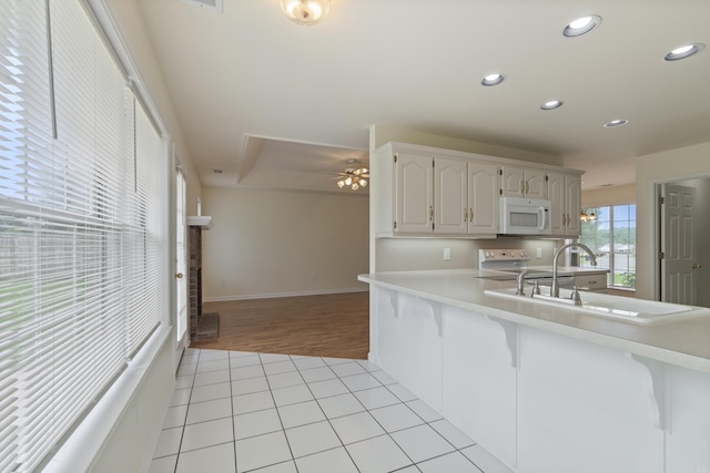 kitchen with white microwave, recessed lighting, light countertops, range, and a kitchen bar