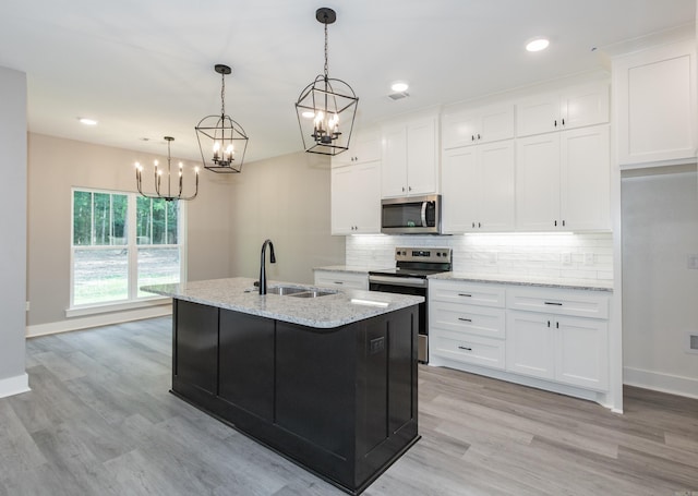 kitchen with stainless steel appliances, a chandelier, decorative backsplash, light wood-style flooring, and an island with sink