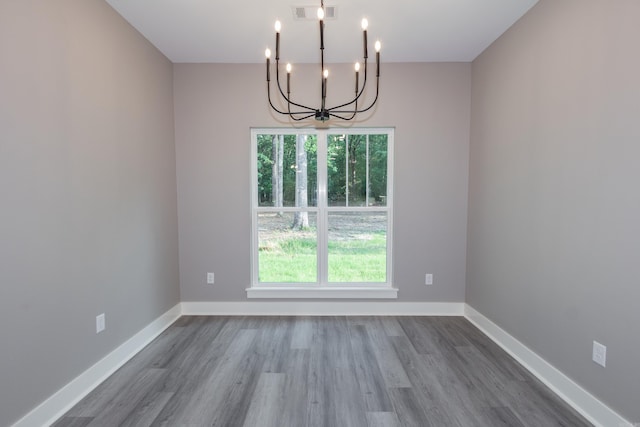 unfurnished room featuring a chandelier, plenty of natural light, and wood finished floors