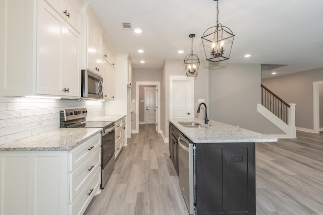 kitchen featuring appliances with stainless steel finishes, white cabinets, tasteful backsplash, light wood-style floors, and a kitchen island with sink