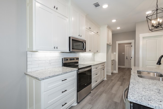 kitchen featuring stainless steel appliances, backsplash, a chandelier, white cabinets, and light wood-style floors