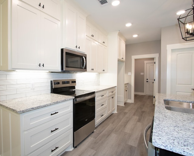 kitchen featuring appliances with stainless steel finishes, a chandelier, decorative backsplash, white cabinetry, and light stone countertops