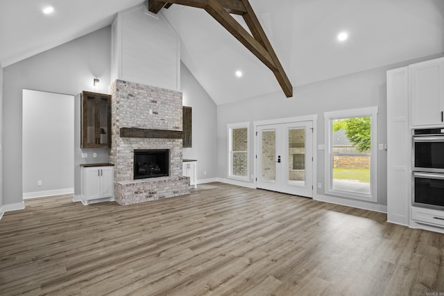 1500 Haley Ln, Conway, AR 72034 - unfurnished living room with high vaulted ceiling, light wood-type flooring, beam ceiling, french doors, and a brick fireplace