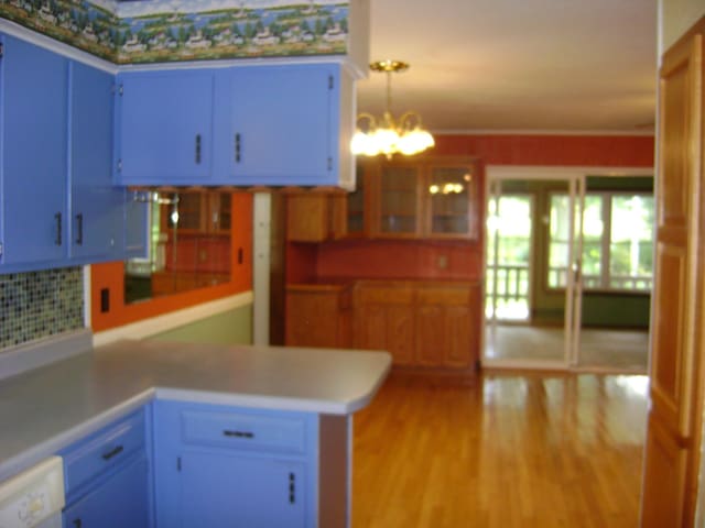 405 Fairway Dr, Horseshoe Bend, AR 72512 - kitchen with blue cabinets, a peninsula, light wood-type flooring, backsplash, and a chandelier