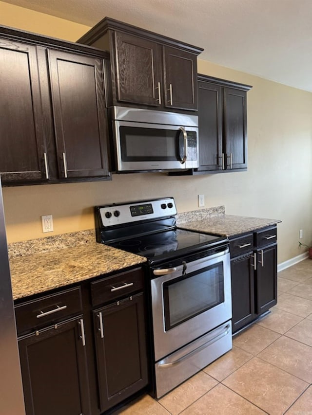 kitchen with stainless steel appliances, light tile patterned floors, dark brown cabinets, and light stone countertops