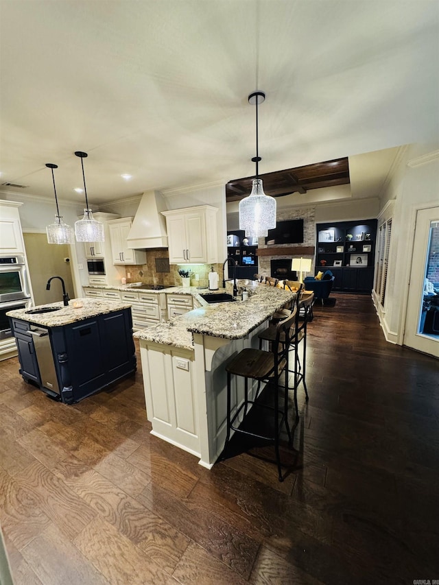 350 Wellesley, Conway, AR 72034 - kitchen with custom exhaust hood, crown molding, an island with sink, a stone fireplace, and dark wood-type flooring
