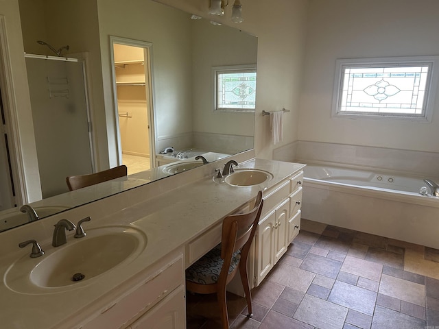 bathroom featuring a bath, a stall shower, double vanity, stone tile flooring, and a walk in closet
