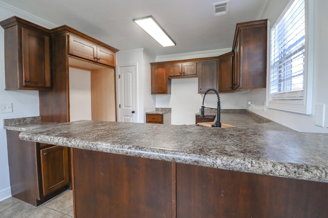 kitchen featuring a peninsula, light tile patterned floors, crown molding, and dark countertops