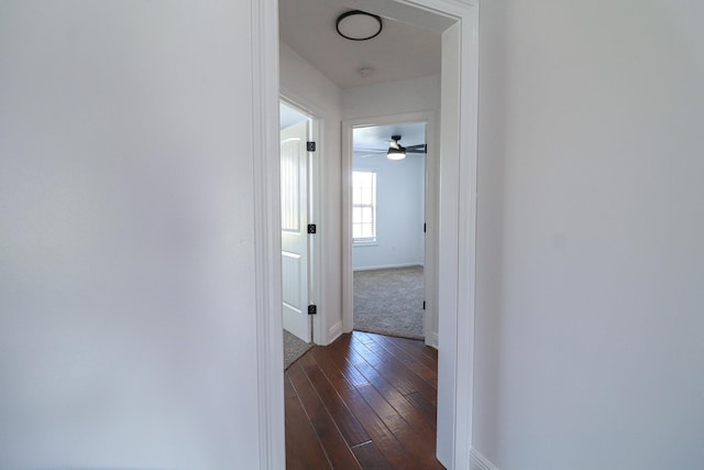 corridor featuring dark wood-type flooring and baseboards