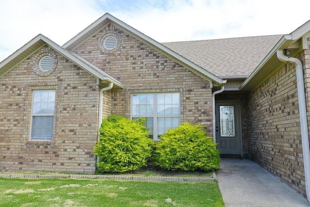 view of exterior entry with brick siding and roof with shingles