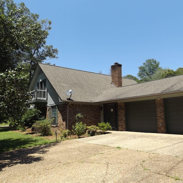 view of front facade with concrete driveway, brick siding, an attached garage, a chimney, and roof with shingles