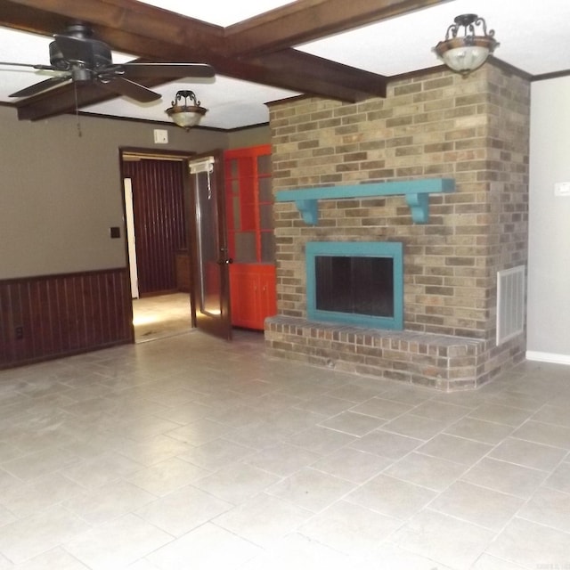 unfurnished living room featuring ceiling fan, a wainscoted wall, beam ceiling, and a fireplace