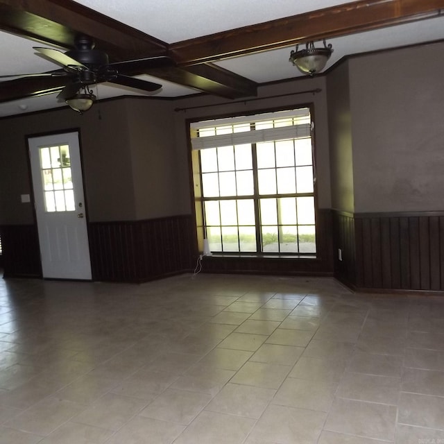 spare room with a wainscoted wall, light tile patterned floors, beam ceiling, a ceiling fan, and wood walls